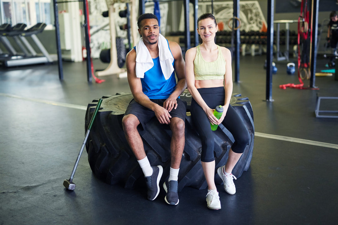 Athletes in activewear sitting on big tyre in front of camera after training in gym