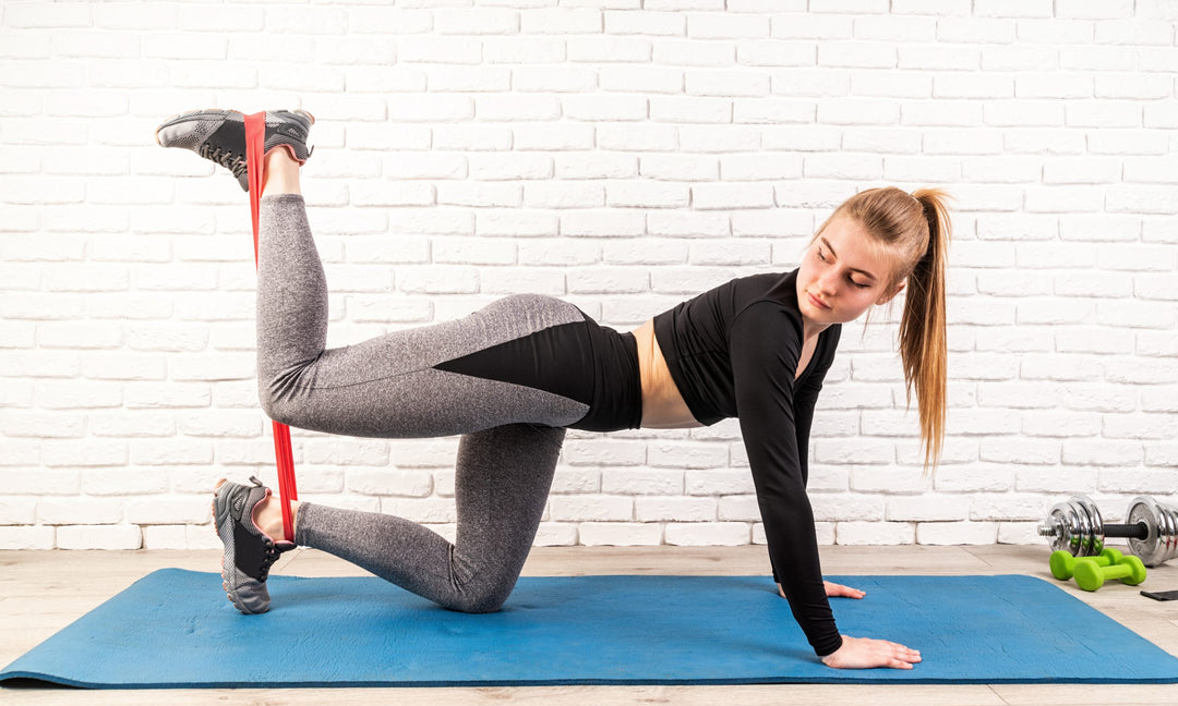 Young sportswoman doing the exercises on all fours arching back straightening leg up at home using rubber resistance band